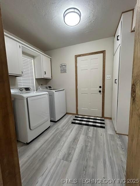 washroom featuring a textured ceiling, washing machine and dryer, cabinet space, baseboards, and light wood-style flooring