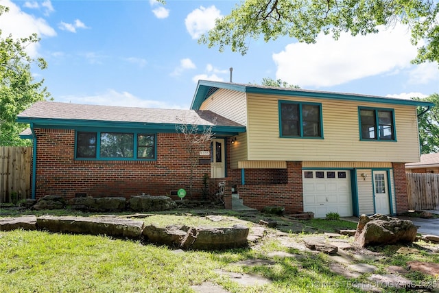 tri-level home with brick siding, a garage, and fence
