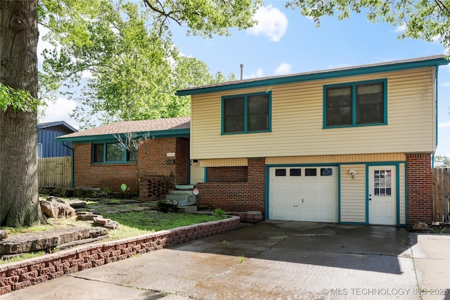 split level home featuring an attached garage, fence, brick siding, and concrete driveway