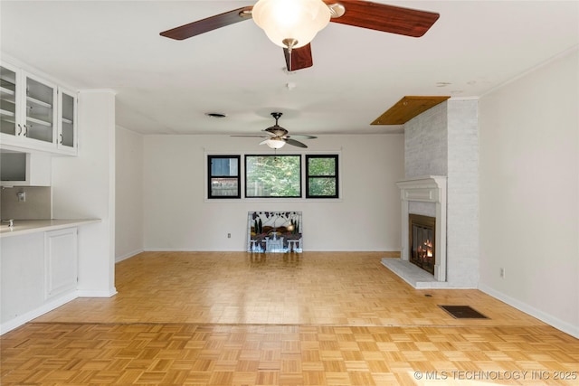 unfurnished living room featuring a ceiling fan, baseboards, visible vents, and a fireplace