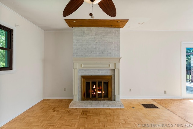 unfurnished living room featuring ceiling fan, a brick fireplace, baseboards, visible vents, and ornamental molding