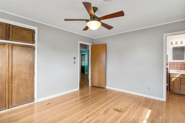 unfurnished bedroom with crown molding, baseboards, connected bathroom, and light wood-style floors
