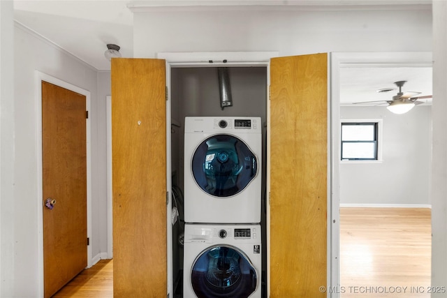 laundry area featuring laundry area, a ceiling fan, stacked washer / dryer, wood finished floors, and baseboards