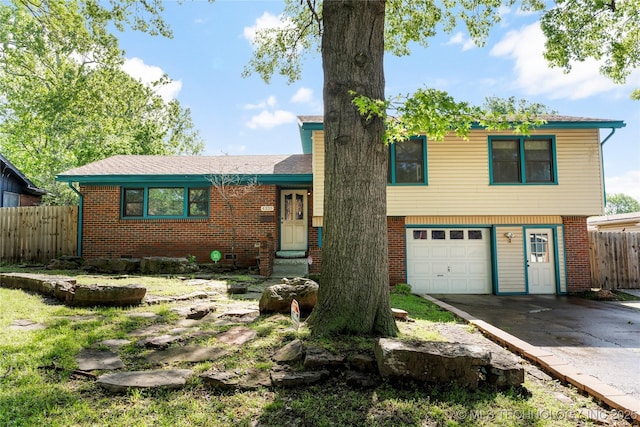 tri-level home featuring a garage, fence, concrete driveway, and brick siding