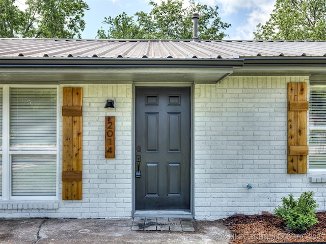 view of exterior entry featuring metal roof and brick siding