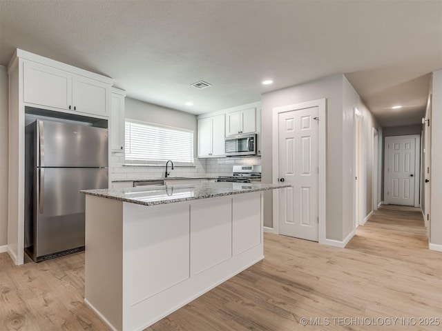 kitchen with decorative backsplash, visible vents, light wood-type flooring, stainless steel appliances, and white cabinetry