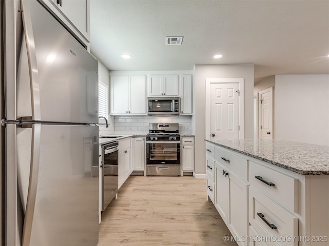 kitchen with visible vents, light wood-type flooring, light stone counters, a sink, and stainless steel appliances