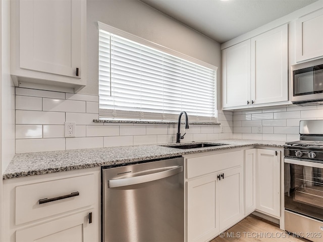 kitchen with light stone countertops, appliances with stainless steel finishes, a sink, white cabinetry, and backsplash