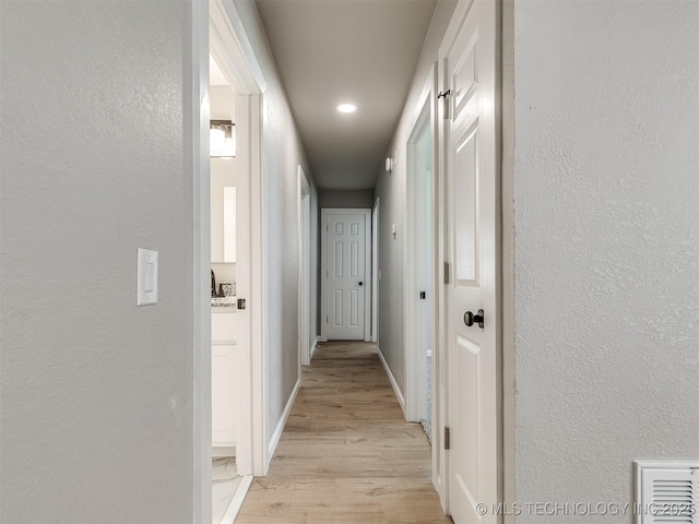 corridor featuring baseboards, light wood finished floors, and a textured wall