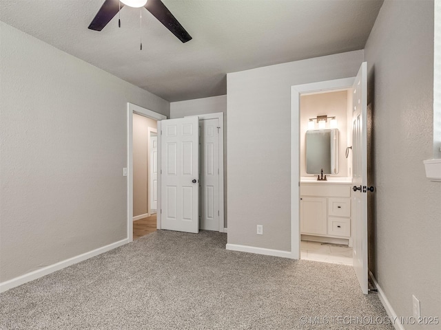 unfurnished bedroom with light carpet, a sink, a ceiling fan, baseboards, and ensuite bathroom