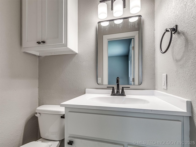 half bath featuring toilet, a textured wall, and vanity