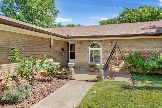 doorway to property featuring a yard, brick siding, and a shingled roof