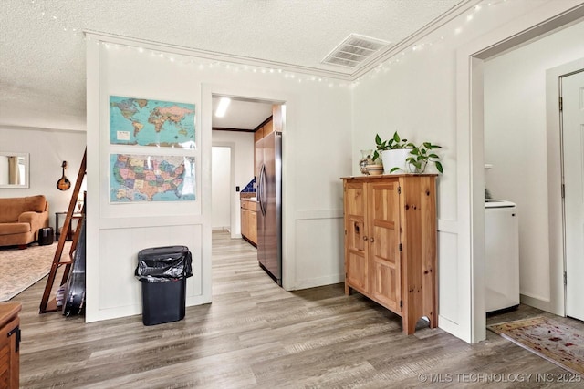 hall featuring a textured ceiling, washer / clothes dryer, light wood-style flooring, and visible vents