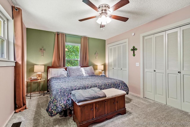 bedroom with a ceiling fan, a textured ceiling, carpet floors, baseboards, and multiple closets