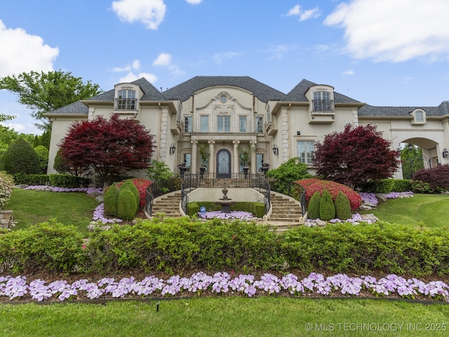 french country style house with stucco siding, stairway, and a front yard