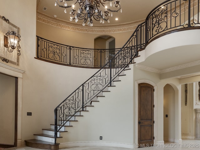 staircase featuring crown molding, visible vents, a high ceiling, a chandelier, and arched walkways