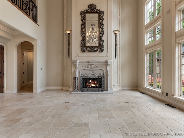 unfurnished living room with arched walkways, a high ceiling, a warm lit fireplace, and stone tile flooring