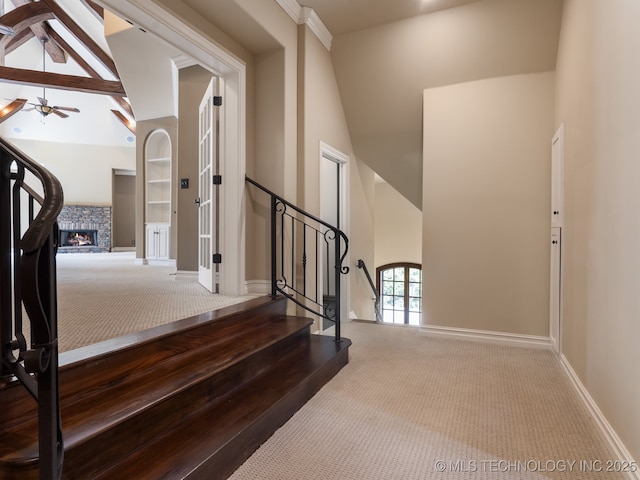 stairs featuring carpet floors, a fireplace, baseboards, ceiling fan, and high vaulted ceiling