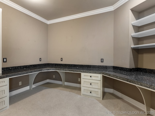 unfurnished office with baseboards, ornamental molding, built in desk, and light colored carpet