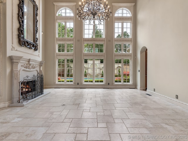 unfurnished living room with baseboards, stone tile flooring, an inviting chandelier, and a towering ceiling