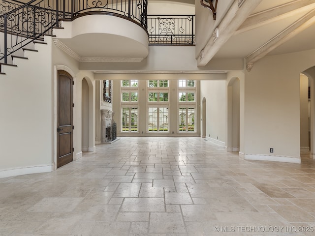 unfurnished living room featuring stone tile flooring, stairs, baseboards, a high ceiling, and arched walkways