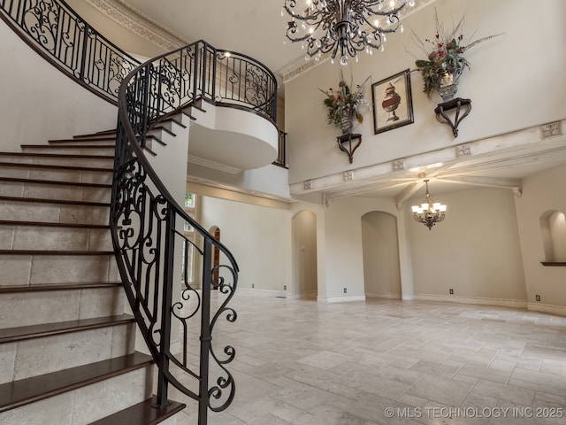 staircase featuring an inviting chandelier, stone tile floors, baseboards, a high ceiling, and arched walkways