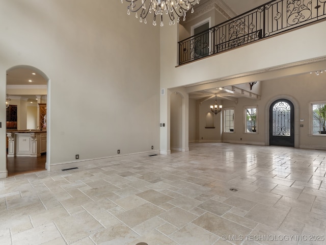 unfurnished living room with an inviting chandelier, stone tile flooring, a towering ceiling, baseboards, and arched walkways