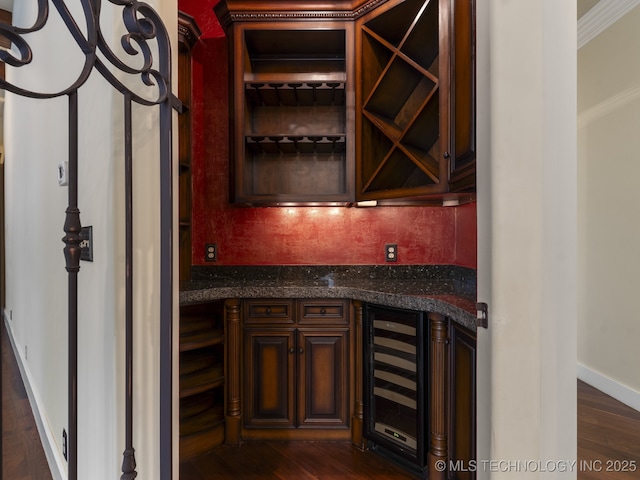 wine room with wine cooler, baseboards, a bar, and dark wood-style flooring