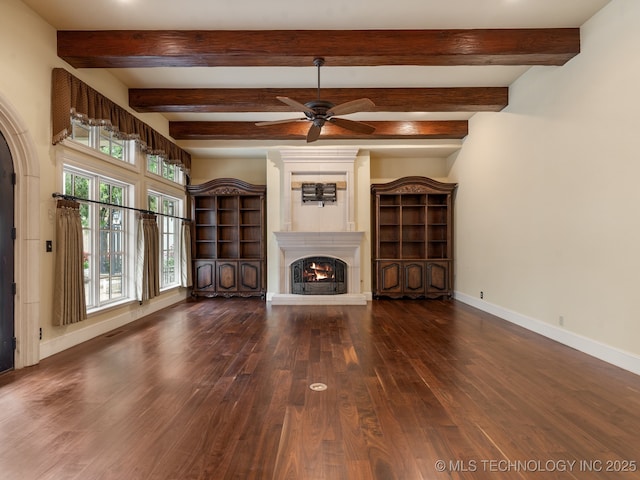 unfurnished living room with a ceiling fan, beam ceiling, wood finished floors, baseboards, and a warm lit fireplace