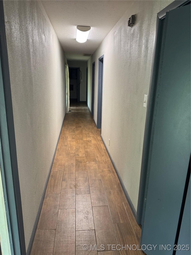 hallway featuring a textured wall, wood finished floors, and visible vents