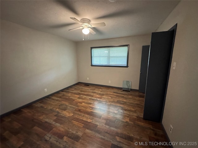 empty room with baseboards, a ceiling fan, dark wood-style floors, and visible vents