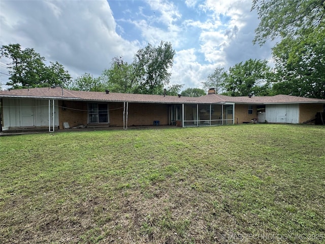 back of house featuring a lawn, a chimney, a sunroom, and brick siding
