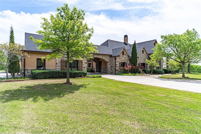view of front of home with a front lawn, stone siding, stucco siding, a chimney, and curved driveway