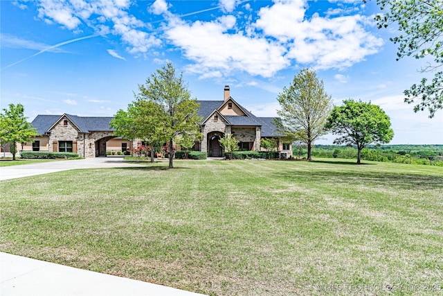 french provincial home with stone siding, a front yard, a chimney, and concrete driveway