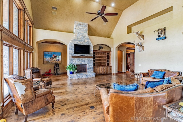 living area featuring ceiling fan, a fireplace, arched walkways, high vaulted ceiling, and wood finished floors