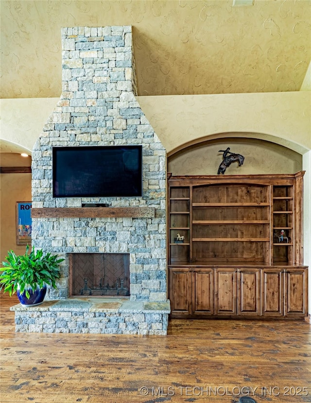 unfurnished living room with a stone fireplace, a textured wall, and wood finished floors