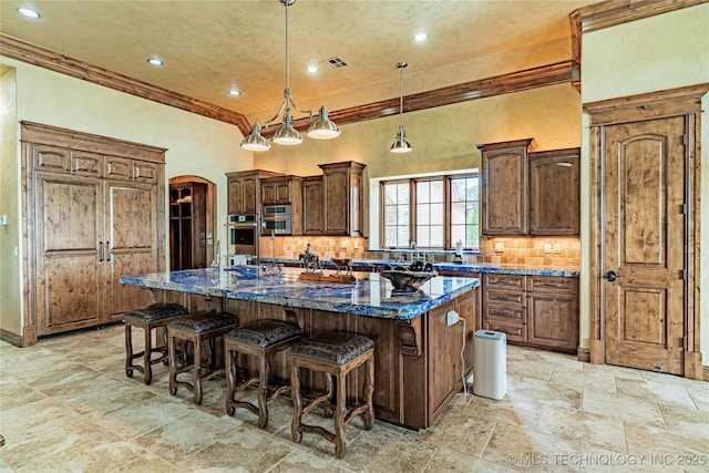 kitchen with arched walkways, stainless steel oven, stone tile floors, a large island, and backsplash