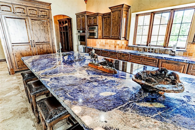 kitchen with a kitchen breakfast bar, black electric stovetop, arched walkways, a sink, and backsplash