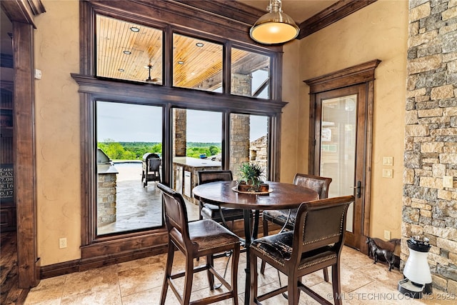 dining area with crown molding, baseboards, and stone tile flooring