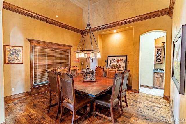 dining room with arched walkways, baseboards, light wood-type flooring, and a towering ceiling