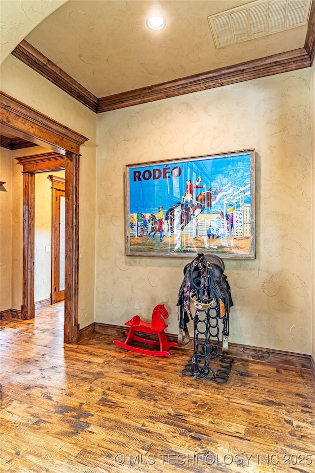 interior space with visible vents, baseboards, crown molding, and wood finished floors