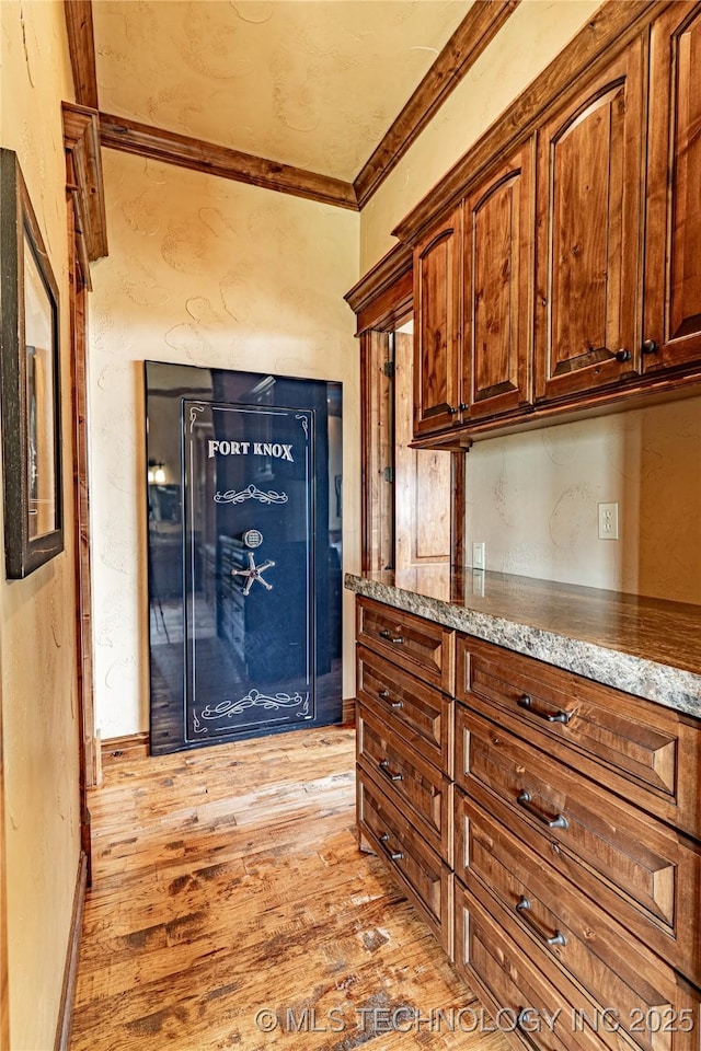 kitchen with light stone counters, ornamental molding, a textured wall, and light wood finished floors