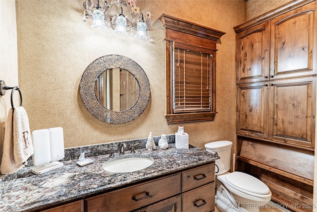 bathroom featuring vanity, a textured wall, toilet, and a notable chandelier