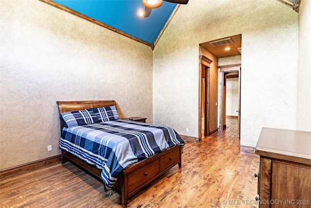bedroom with visible vents, baseboards, lofted ceiling, ornamental molding, and hardwood / wood-style floors