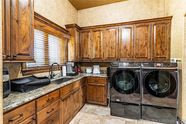 clothes washing area featuring stone finish flooring, washing machine and dryer, cabinet space, a sink, and a textured wall