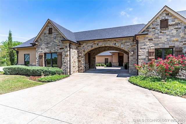 french country style house with concrete driveway, a shingled roof, and stone siding