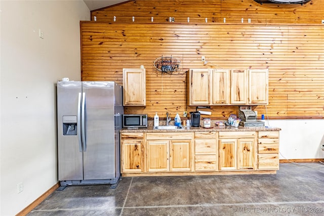 kitchen featuring appliances with stainless steel finishes, light brown cabinetry, wood walls, a sink, and lofted ceiling