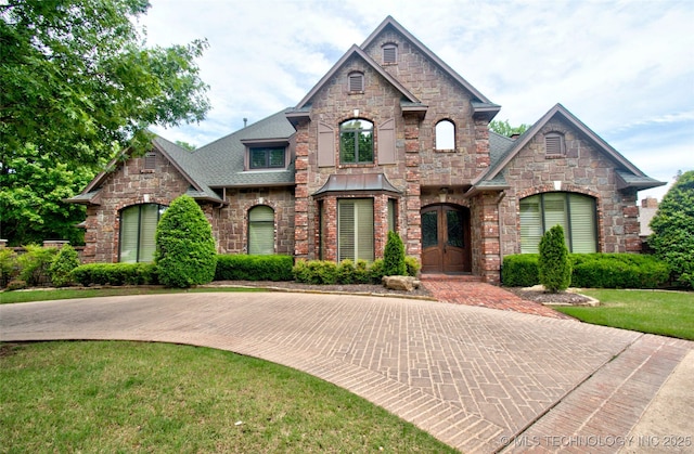 french country style house with a shingled roof, a front lawn, french doors, and stone siding