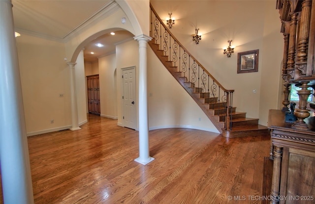 interior space featuring arched walkways, ornamental molding, wood finished floors, and stairway