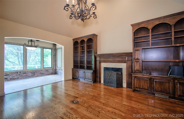 unfurnished living room with visible vents, wood finished floors, a fireplace, a chandelier, and arched walkways